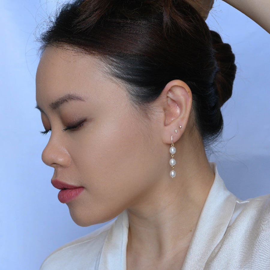 Close-up of a woman wearing pearl earrings with a plain background